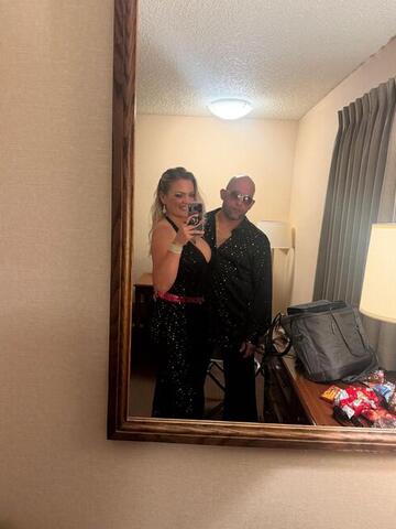 Commander and Night Shade reflected in a hotel room mirror, both in black sequinned outfits
