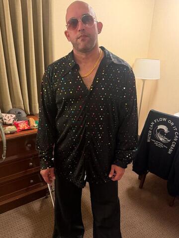 Commander standing in a hotel room in a black sequinned suit wearing sunglasses