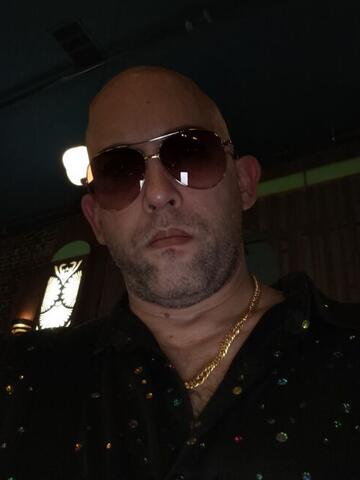 Commander at night in a dark venue wearing aviator sunglasses and a sequinned shirt