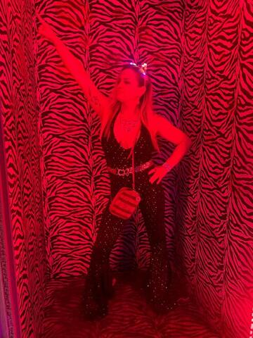 Night Shade with one arm raised in a red-lit zebra-print photo corridor