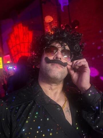 Commander adjusting his fake moustache with both hands in a dark club