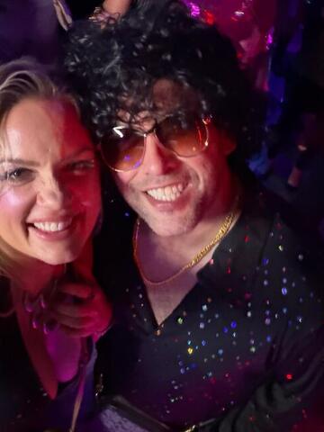 Commander in a curly wig and Night Shade smiling together in a dark club