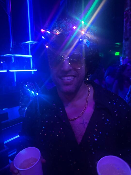 Commander lit by blue laser beams in a dark club, sequins catching the light