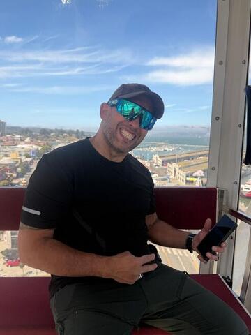 Commander seated in a Ferris wheel cabin holding a phone with the city behind him
