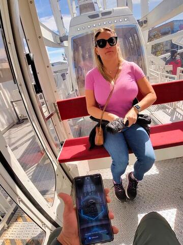 Night Shade leaning forward with a phone inside a Ferris wheel cabin