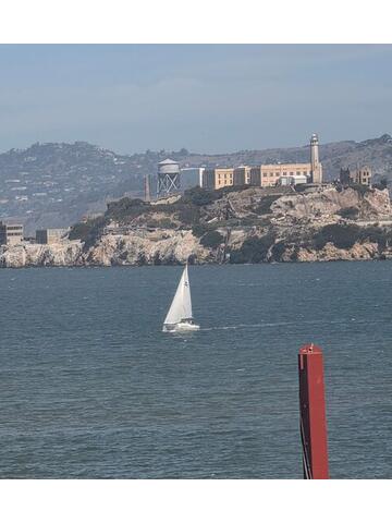 Alcatraz Island in the bay with a white sailboat in the foreground