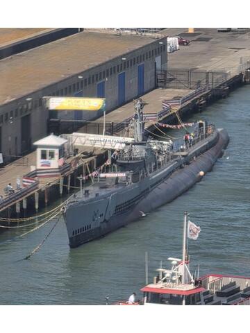 A grey World War Two submarine moored at a pier with a tugboat alongside