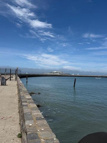 A long concrete pier curving out into the bay under a blue sky