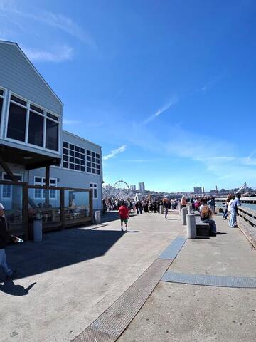 A waterfront boardwalk with people walking and a Ferris wheel in the distance
