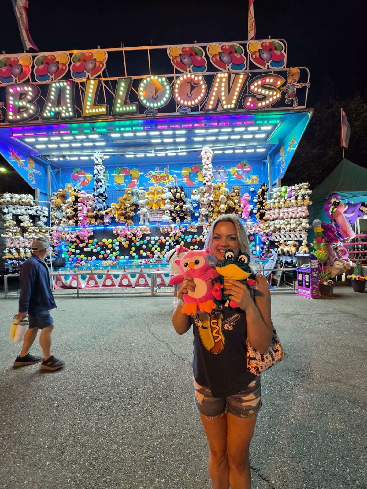 Night Shade holding plush owl and frog prizes in front of balloon dart booth